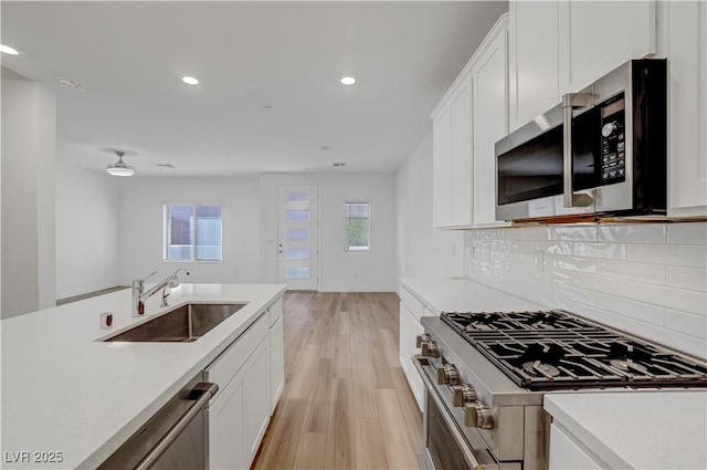 kitchen with stainless steel appliances, light hardwood / wood-style floors, backsplash, white cabinetry, and sink