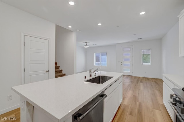 kitchen with sink, an island with sink, stainless steel dishwasher, and white cabinetry