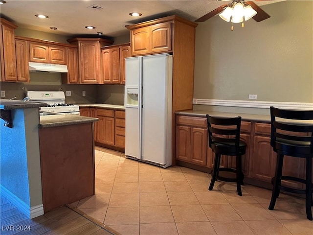 kitchen with a breakfast bar, ceiling fan, white appliances, and light tile patterned floors