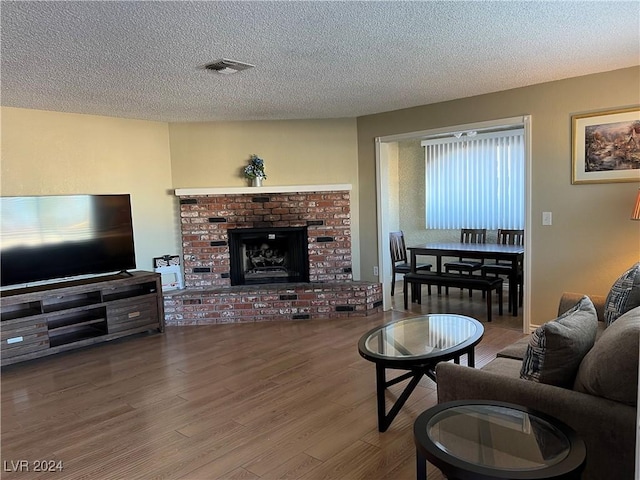 living room with a textured ceiling, hardwood / wood-style flooring, and a brick fireplace