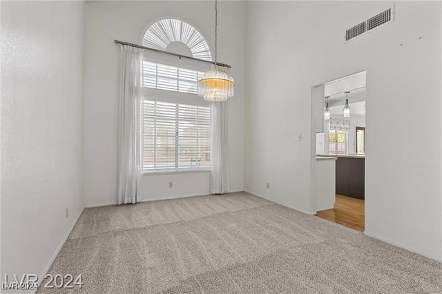 unfurnished room featuring carpet floors, a towering ceiling, and a chandelier