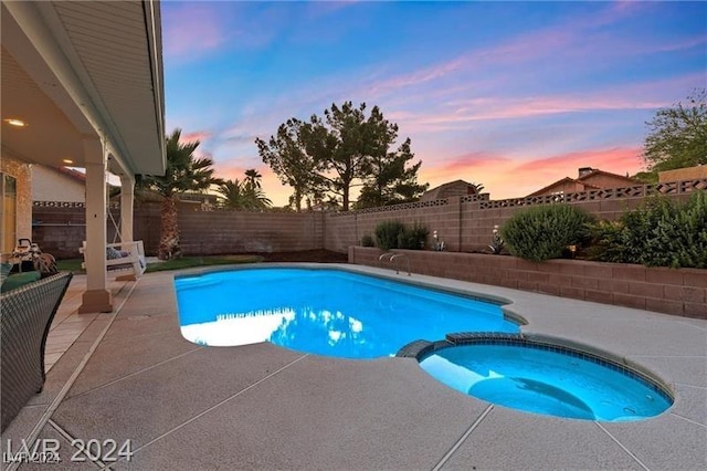 pool at dusk featuring an in ground hot tub and a patio