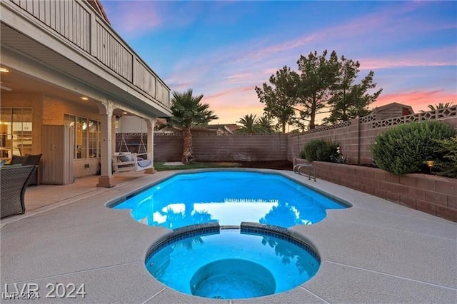 pool at dusk featuring a patio area and an in ground hot tub