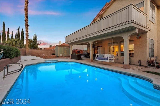 pool at dusk with a patio area and a storage shed