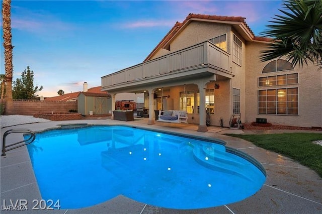 pool at dusk featuring a patio and a shed