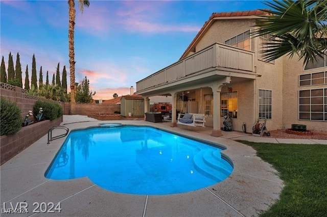 pool at dusk with a patio area and a storage shed