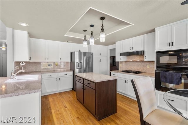 kitchen featuring pendant lighting, sink, light wood-type flooring, a kitchen island, and white cabinetry