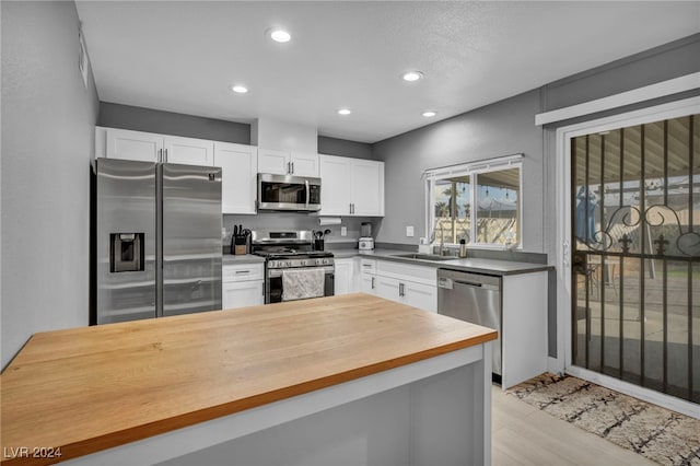 kitchen with white cabinets, sink, light hardwood / wood-style flooring, appliances with stainless steel finishes, and butcher block counters