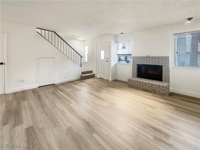 unfurnished living room featuring a fireplace, a textured ceiling, and light wood-type flooring