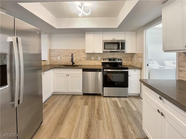 kitchen with appliances with stainless steel finishes, a tray ceiling, sink, independent washer and dryer, and white cabinetry