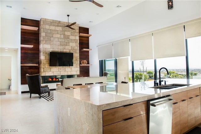 kitchen featuring light stone counters, ceiling fan, sink, a multi sided fireplace, and a center island