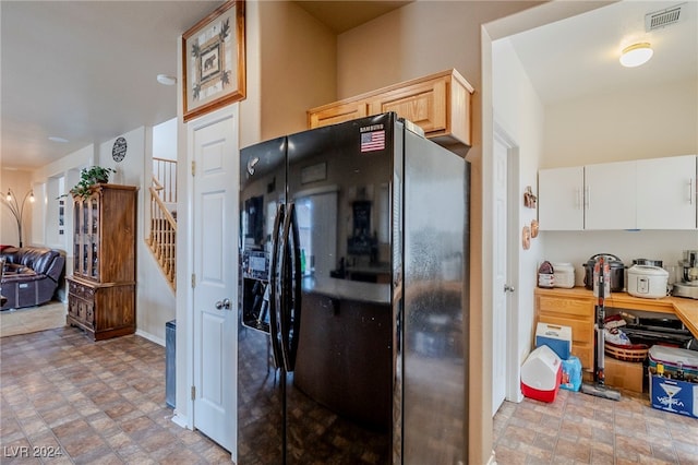 kitchen featuring white cabinets, light brown cabinetry, and black fridge