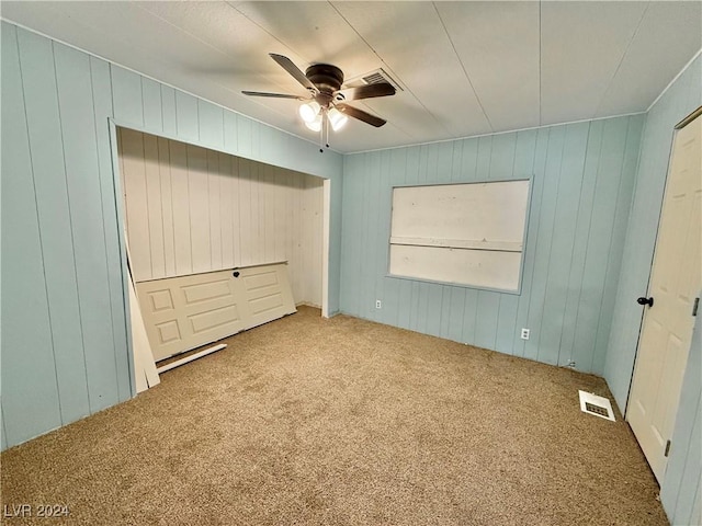 unfurnished bedroom featuring carpet flooring, ceiling fan, and wood walls