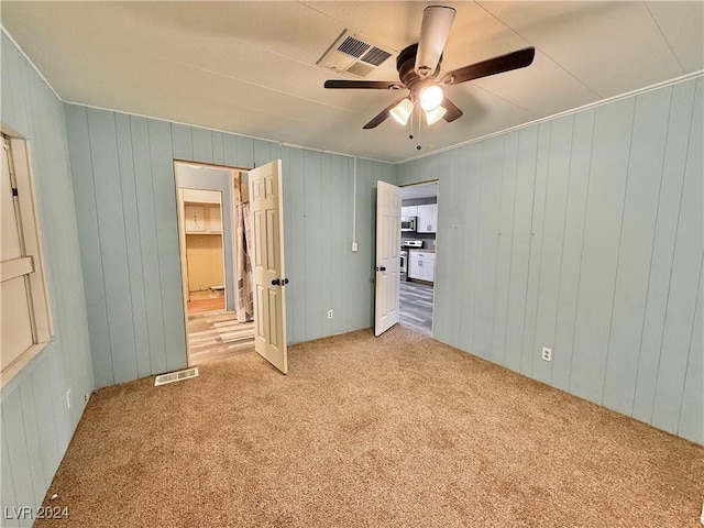 unfurnished bedroom featuring carpet, a spacious closet, ceiling fan, and wood walls