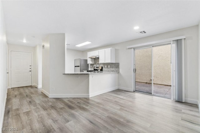 kitchen with kitchen peninsula, stainless steel fridge, white cabinetry, and a healthy amount of sunlight