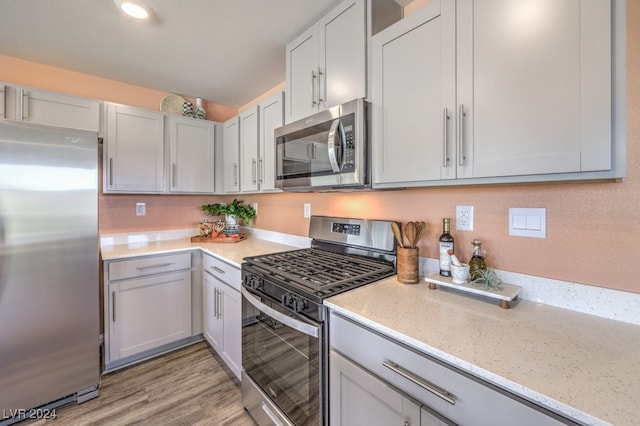 kitchen with a textured ceiling, light stone countertops, stainless steel appliances, and light hardwood / wood-style flooring