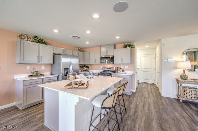 kitchen featuring an island with sink, gray cabinets, a breakfast bar, appliances with stainless steel finishes, and hardwood / wood-style flooring