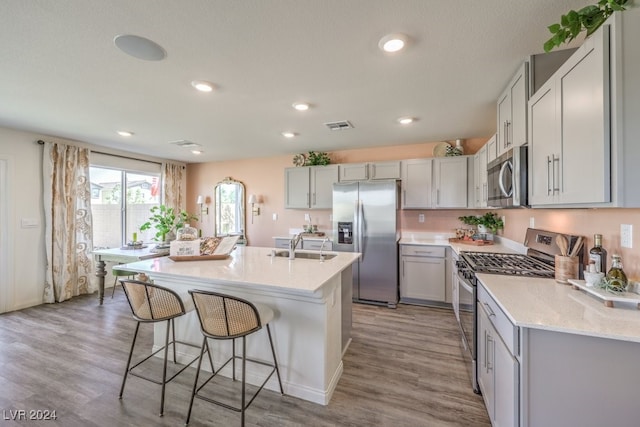 kitchen with sink, an island with sink, appliances with stainless steel finishes, light hardwood / wood-style floors, and a breakfast bar area