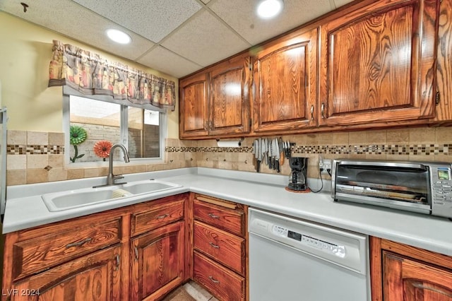 kitchen with a paneled ceiling, white dishwasher, backsplash, and sink