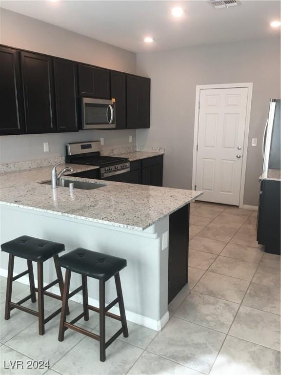 kitchen featuring a breakfast bar, light stone countertops, kitchen peninsula, and appliances with stainless steel finishes