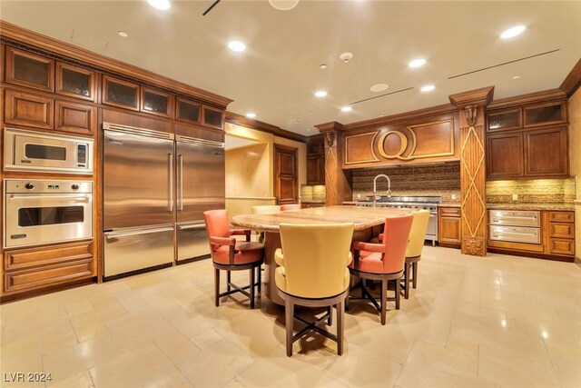 kitchen with built in appliances, crown molding, an island with sink, a breakfast bar area, and decorative backsplash