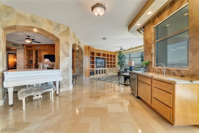 kitchen featuring sink, ceiling fan, light stone countertops, light brown cabinetry, and beverage cooler