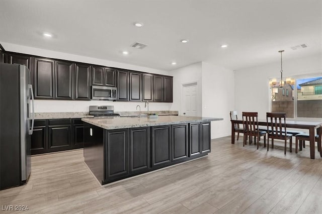 kitchen with light stone counters, an island with sink, light hardwood / wood-style floors, pendant lighting, and appliances with stainless steel finishes