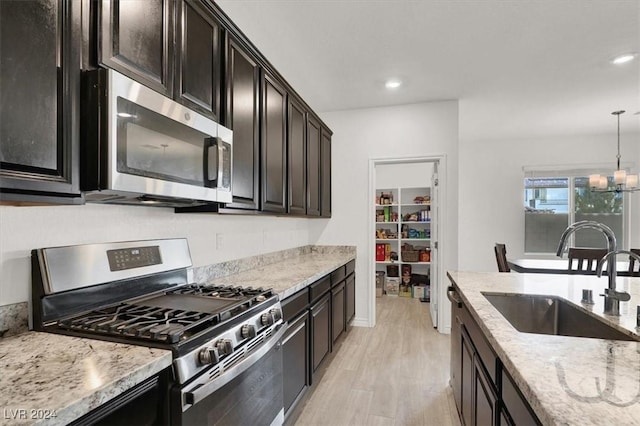 kitchen featuring sink, stainless steel appliances, an inviting chandelier, decorative light fixtures, and light wood-type flooring