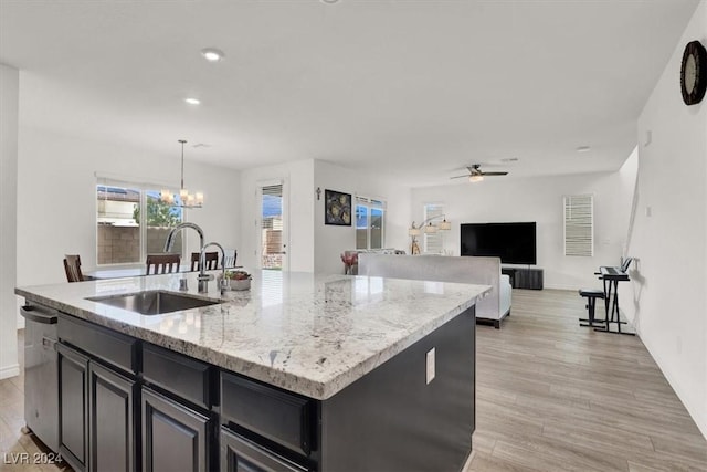 kitchen with sink, hanging light fixtures, a center island with sink, ceiling fan with notable chandelier, and light wood-type flooring