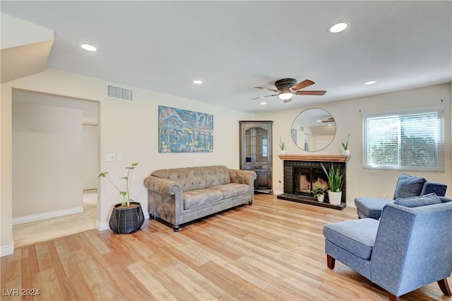 living room with ceiling fan, a fireplace, and light hardwood / wood-style floors