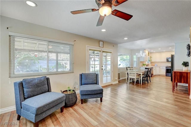 living area featuring french doors, light hardwood / wood-style floors, ceiling fan with notable chandelier, and sink