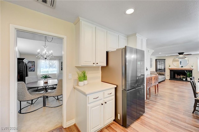 kitchen featuring light wood-type flooring, a brick fireplace, white cabinets, stainless steel refrigerator, and hanging light fixtures