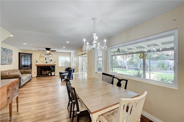 dining area featuring ceiling fan with notable chandelier, light hardwood / wood-style floors, a brick fireplace, and a healthy amount of sunlight