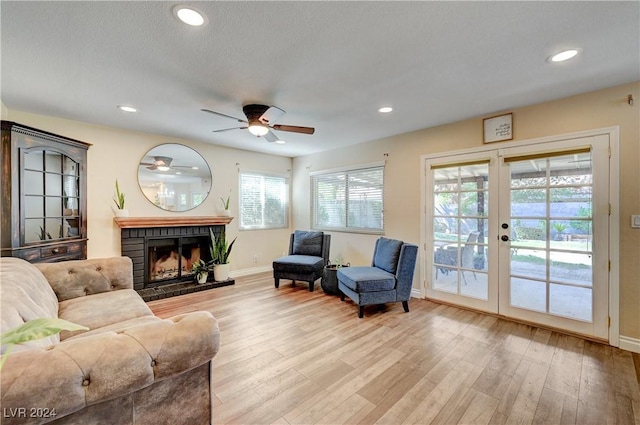 living room featuring ceiling fan, light hardwood / wood-style floors, french doors, and a brick fireplace