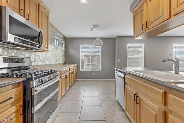 kitchen featuring pendant lighting, backsplash, sink, appliances with stainless steel finishes, and light tile patterned flooring