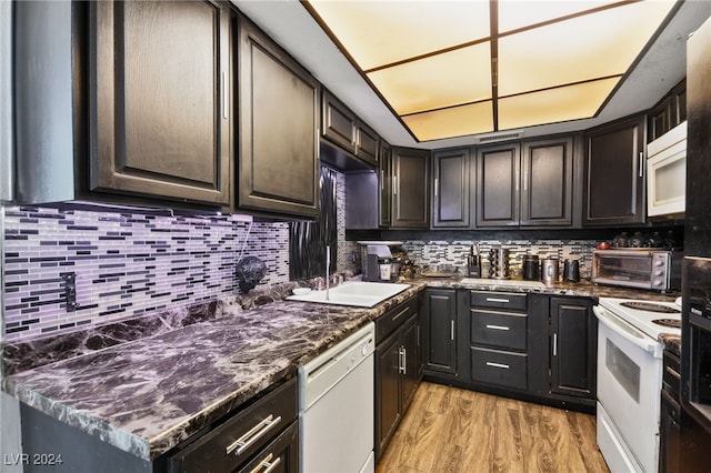 kitchen featuring white appliances, dark stone countertops, decorative backsplash, and light wood-type flooring