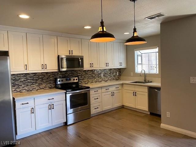 kitchen featuring appliances with stainless steel finishes, sink, pendant lighting, hardwood / wood-style floors, and white cabinetry