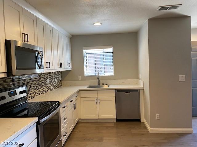 kitchen featuring backsplash, white cabinets, sink, light wood-type flooring, and stainless steel appliances