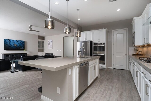 kitchen with an island with sink, white cabinets, stainless steel appliances, and hanging light fixtures