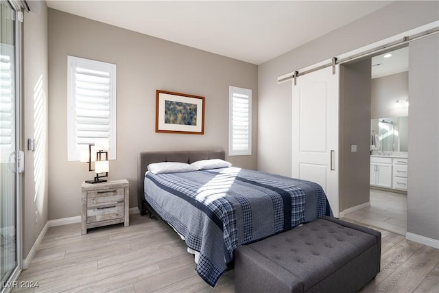 bedroom with ensuite bathroom, light hardwood / wood-style floors, and a barn door