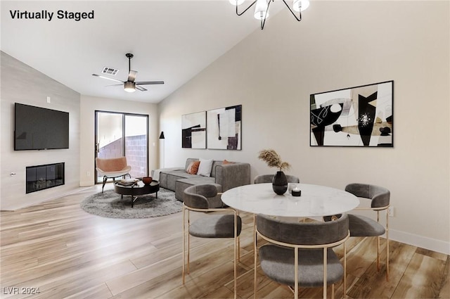 dining room featuring ceiling fan with notable chandelier, light hardwood / wood-style floors, and vaulted ceiling