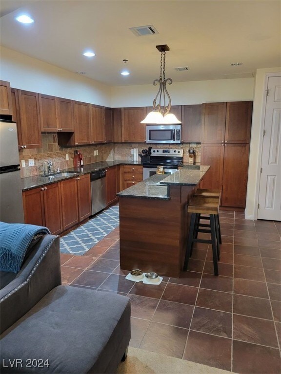 kitchen featuring appliances with stainless steel finishes, backsplash, pendant lighting, dark tile patterned flooring, and a center island