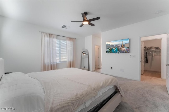 bedroom with a walk in closet, a closet, ceiling fan, and light colored carpet