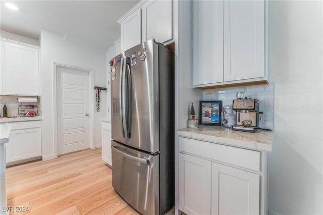 kitchen featuring white cabinets, stainless steel fridge, light wood-type flooring, and backsplash