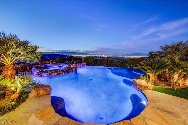 pool at dusk featuring a mountain view and an in ground hot tub