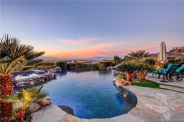 pool at dusk featuring a jacuzzi, pool water feature, a mountain view, and a patio