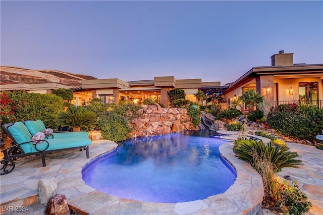 pool at dusk featuring pool water feature and a patio