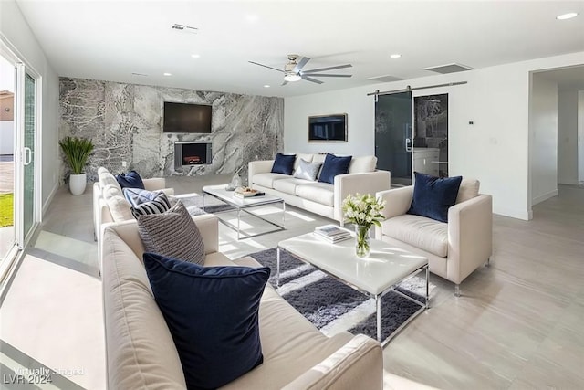 living room with a high end fireplace, ceiling fan, a barn door, and a wealth of natural light