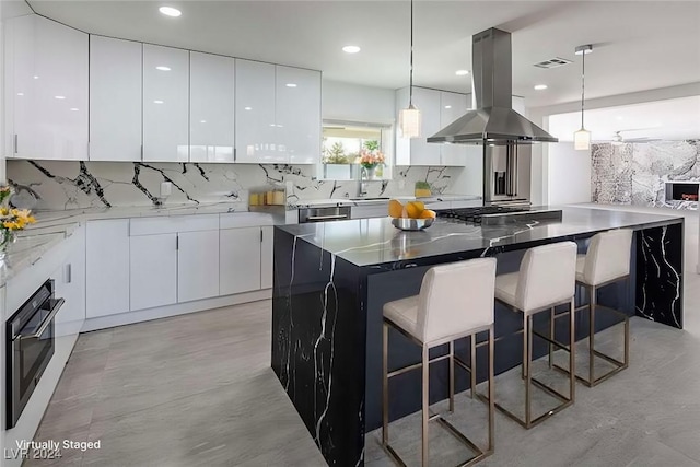 kitchen with island exhaust hood, appliances with stainless steel finishes, decorative backsplash, a kitchen island, and white cabinetry