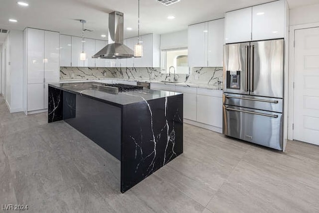 kitchen featuring high end refrigerator, white cabinetry, a kitchen island, and wall chimney range hood